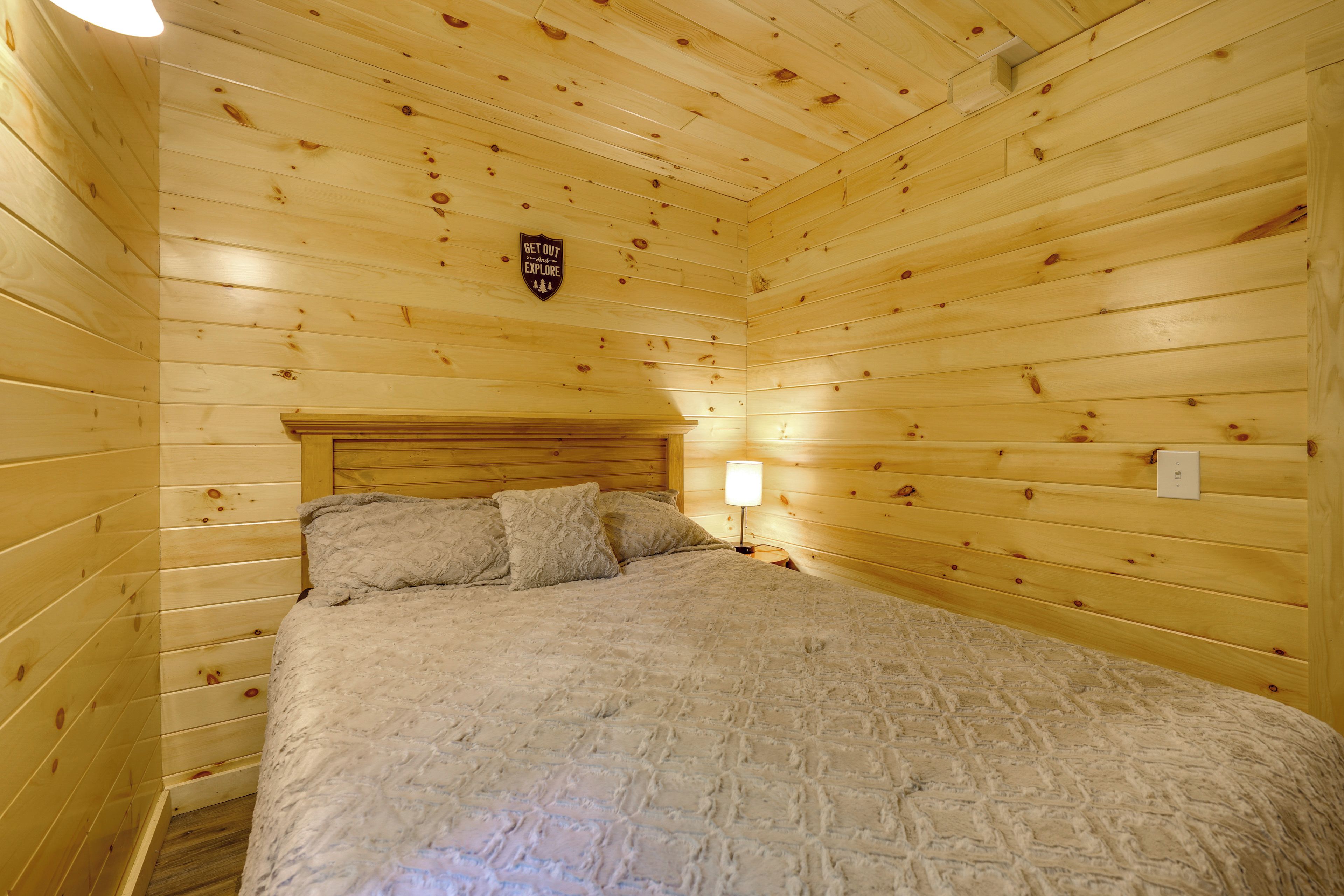 A wooden cabin room with a bed, a nightstand, a lamp, and a sign on the wall.