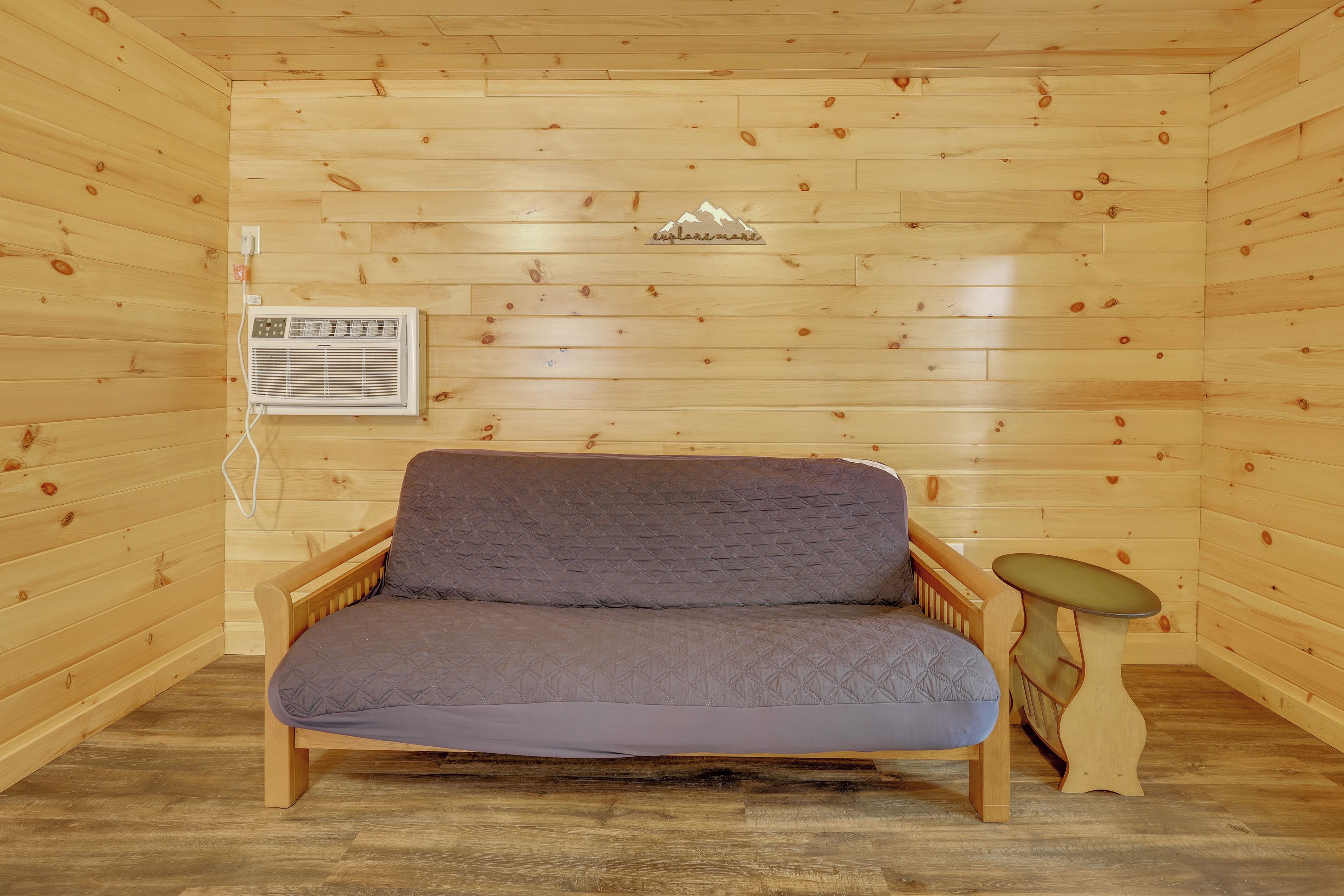 Quarto de cabana de madeira com sofá, uma mesinha e um ar condicionado.