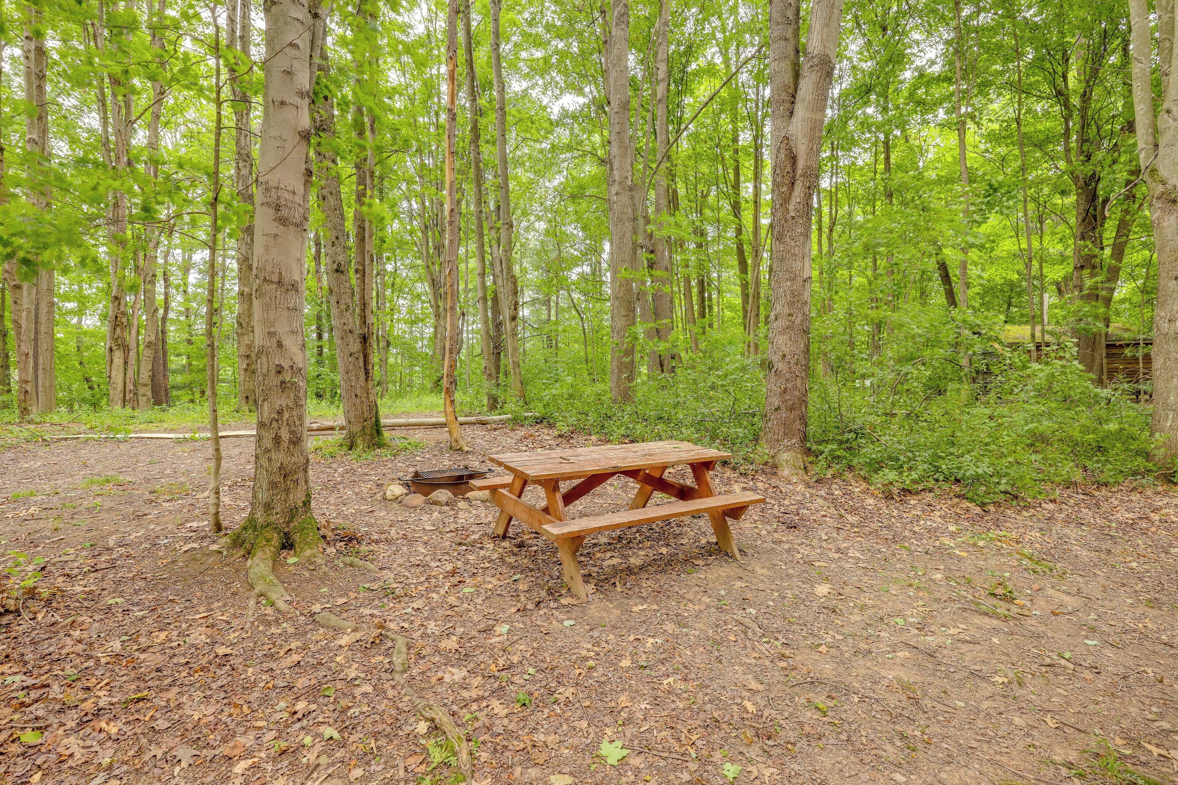 Una mesa de picnic en un bosque con árboles y un brasero cerca.