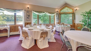 Een balzaal met ronde tafels, witte tafelkleden en stoelen met beige linten.