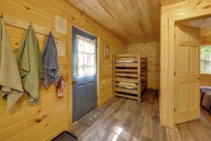 Interior de una cabaña con una puerta de madera, un extintor, una cama litera y un perchero.
