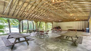 An outdoor pavilion with picnic tables and chairs, a stage, and a view of a lake.