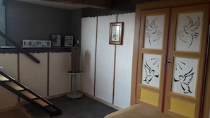 A room with a wooden staircase, a wall-mounted picture frame, and a door with decorative panels. - Brocéliande East Vacation Rental (Iffendic)