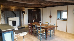A dining area with a wooden table, colorful chairs, a white chair, a black stove, and a decorative rooster.