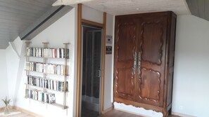 A room with a wooden door, a bookshelf filled with books, and a small plant. - Brocéliande East Vacation Rental (Iffendic)