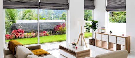 A modern living room with a sofa, coffee table, and a view of a garden through large windows.