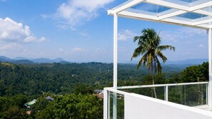 Un edificio moderno con un balcón de cristal que da a un paisaje verde exuberante y montañas distantes.