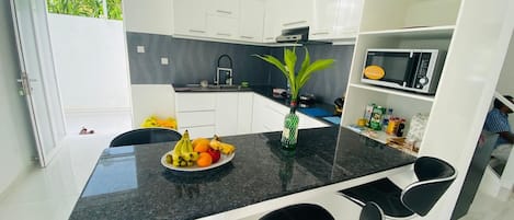 A modern kitchen with white cabinets, a black countertop, and a fruit bowl.