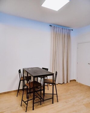 A room with a wooden floor, a table with chairs, a window with curtains, and a door. - Regina Anna Home (Bari)