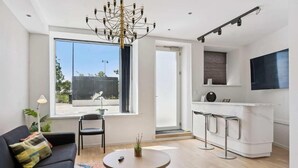 Un espace de vie moderne comprenant un canapé, une table basse ronde, un coin repas avec un bar blanc et une grande fenêtre.