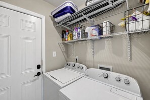 A laundry room with two stacked washers and dryers, shelves above holding various laundry supplies, and a white door. - Renovated 3-bedroom house in Martinez (Martinez)