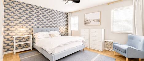 Une chambre à coucher comprenant un lit, des tables de chevet, une chaise, une armoire et un ventilateur de plafond.