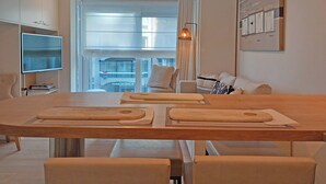 A modern living room with a dining area, a flat-screen TV, and a large window with curtains. - Coastal Family Escape in Knokke (Knokke-Heist)