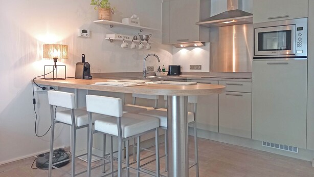 A modern kitchen with a central island, bar stools, a built-in oven, and a microwave. - Coastal Family Escape in Knokke (Knokke-Heist)