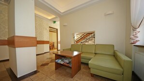 A hotel lobby with a green sofa, a wooden coffee table, and a tiled floor. - Zamkowy (Slupsk)
