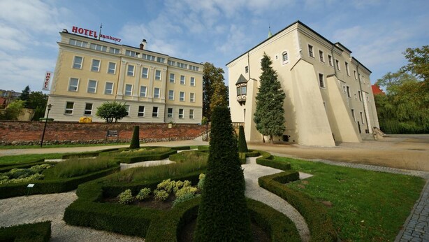 A hotel building with a sign reading 'HOTEL zamkowy' and a well-maintained garden with hedges and a central tree. - Zamkowy (Slupsk)