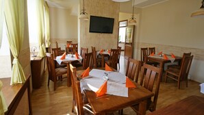 A dining area with wooden tables and chairs, a flat-screen TV mounted on the wall, and a window with curtains. - Zamkowy (Slupsk)