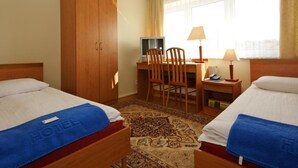 A hotel room with two beds, a desk, a chair, a television, and a large window with curtains. - Zamkowy (Slupsk)