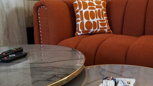 Un salon avec une table basse ronde en verre, un canapé agrémenté d’un coussin à motifs de girafe et une télécommande posée sur la table.