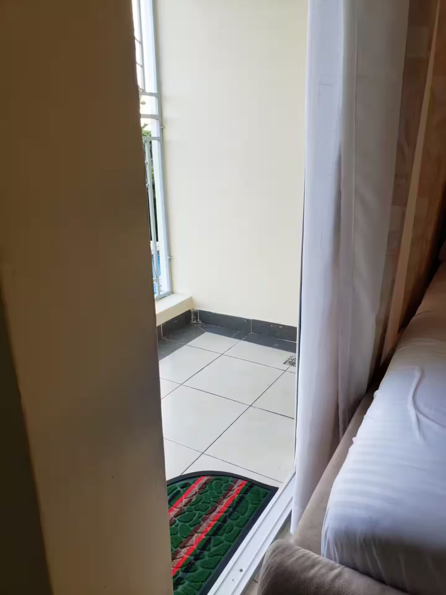 A room with a bed, a window, and a view of a tiled balcony area.