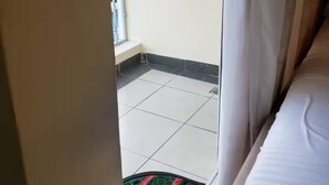 Une chambre avec un lit, une fenêtre et une vue sur un balcon carrelé.
