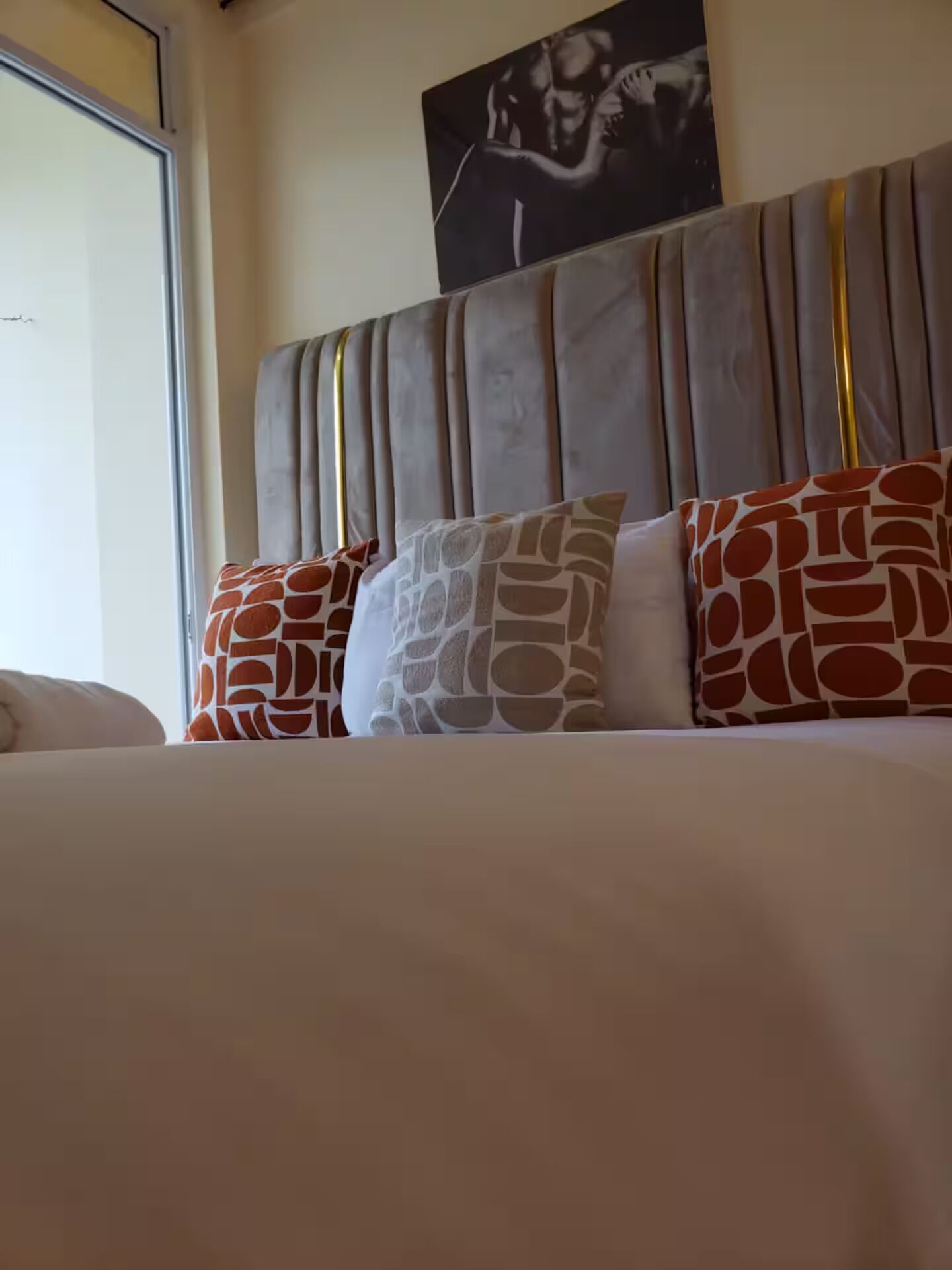 Uma cama com cabeceira, várias almofadas estampadas e um quadro na parede.