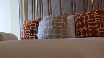 Uma cama com cabeceira, várias almofadas estampadas e um quadro na parede.
