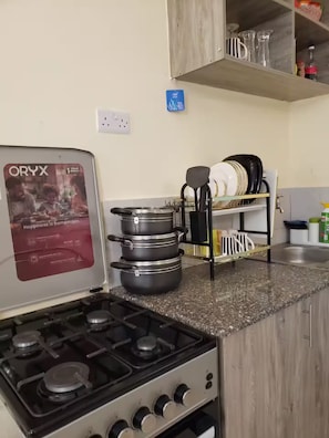 A kitchen with a gas stove, pots, a coffee maker, and a dish rack.