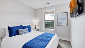 A hotel room with a bed, a nightstand, a lamp, a window with a view, and a painting on the wall. - Grill-Mnt Views-Private Hot Tub-King Bed-Sleeps 12 | Moose Mgmt 1132 (Park City)