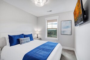 A hotel room with a bed, a nightstand, a lamp, a window with a view, and a painting on the wall. - Grill-Mnt Views-Private Hot Tub-King Bed-Sleeps 12 | Moose Mgmt 1132 (Park City)
