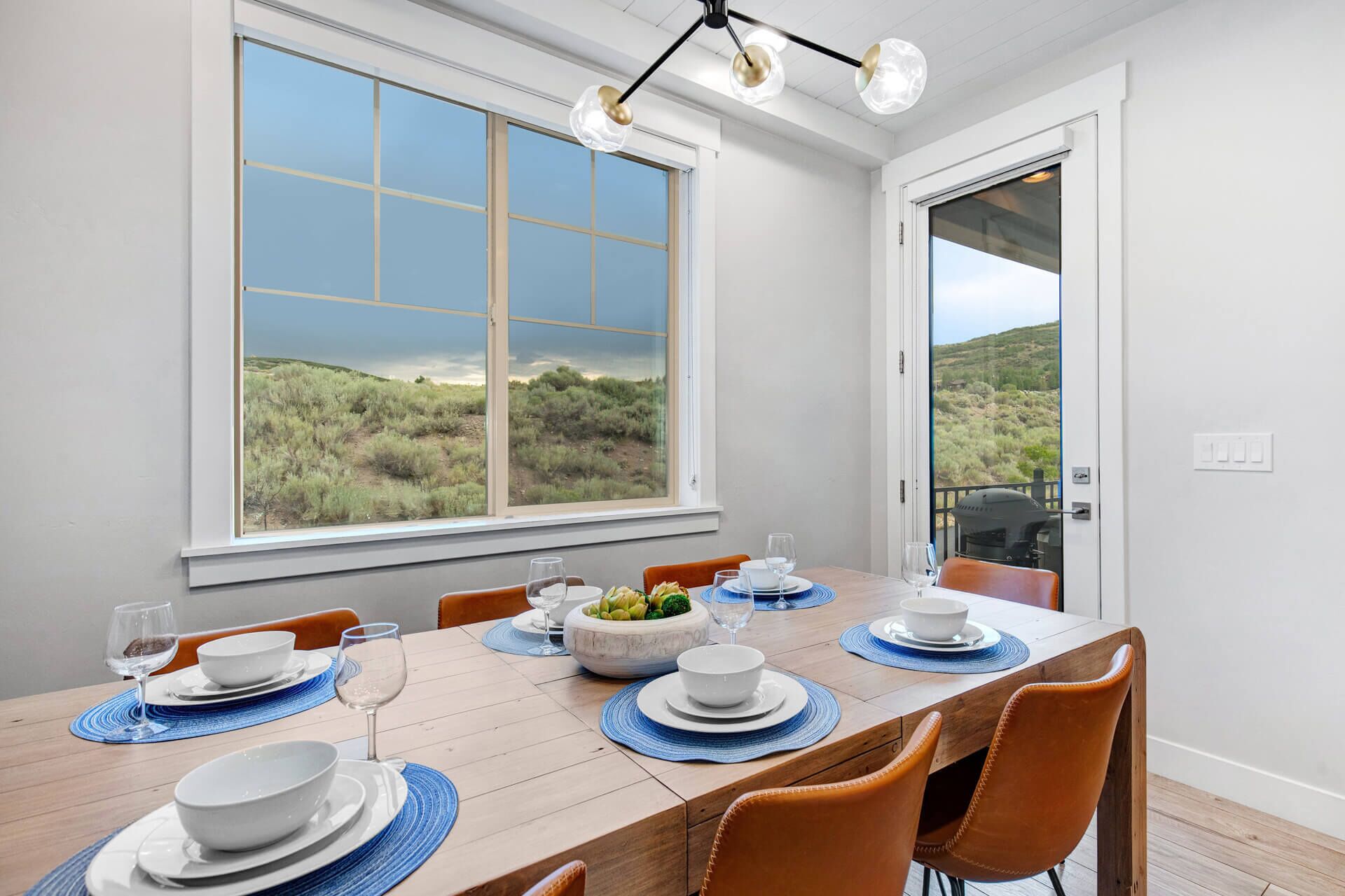 A dining area with a table set for four, large windows with a view of a landscape, and a ceiling light fixture.