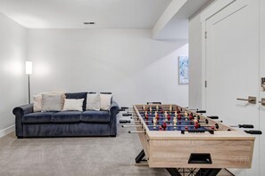 A room with a dark blue sofa, a foosball table, a floor lamp, and a door with a keypad lock. - Grill-Mnt Views-Private Hot Tub-King Bed-Sleeps 12 | Moose Mgmt 1132 (Park City)