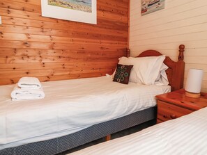 A wooden-paneled room with a bed, a nightstand, and a lamp. - Seagull Lodge (Ilfracombe)