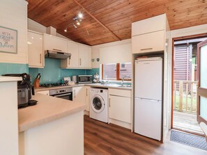 A compact kitchen with a washing machine, a microwave, and a refrigerator. - Seagull Lodge (Ilfracombe)
