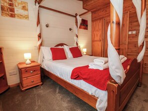 A wooden four-poster bed with white linens and red pillows, a nightstand with a lamp, and a wooden wardrobe. - Seagull Lodge (Ilfracombe)