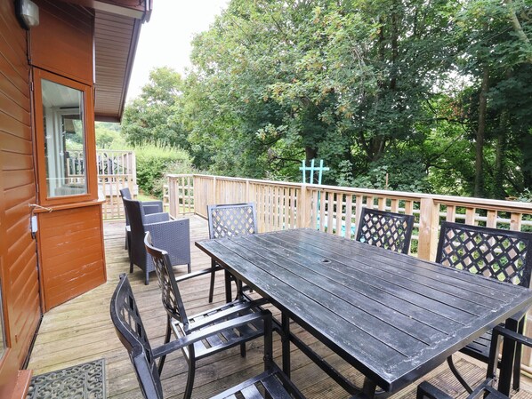 A wooden deck with a table and chairs, surrounded by a wooden fence and trees. - Seagull Lodge (Ilfracombe)