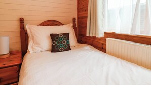 A wooden-paneled room with a bed, a nightstand, a lamp, and a window with curtains. - Seagull Lodge (Ilfracombe)