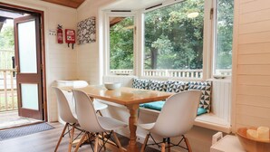 A dining area with a wooden table, white chairs, and a bench with patterned cushions. - Seagull Lodge (Ilfracombe)