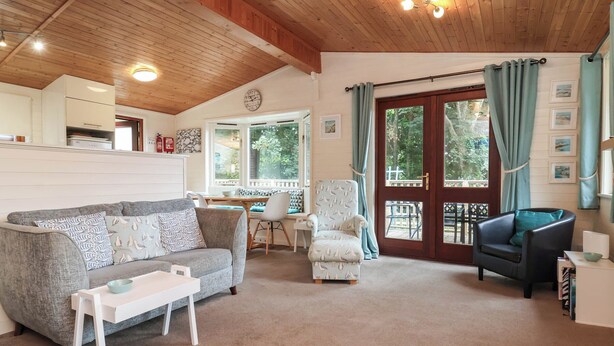 A cozy living room with a sofa, armchairs, a small table, and a dining area with a window. - Seagull Lodge (Ilfracombe)