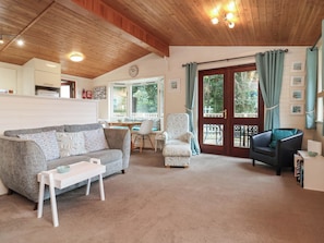 A cozy living room with a sofa, armchairs, a small table, and a dining area with a window. - Seagull Lodge (Ilfracombe)