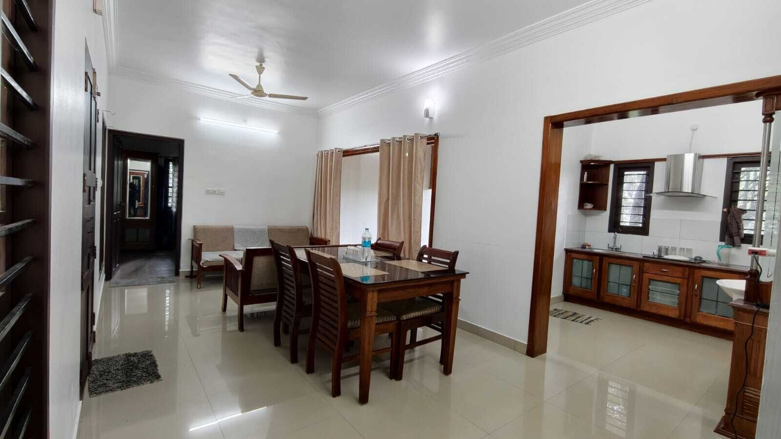A dining area with a wooden table and chairs, a sofa, and a kitchen area with cabinets and a countertop.