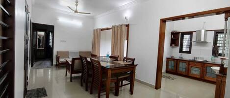 A dining area with a wooden table and chairs, a sofa, and a kitchen area with cabinets and a countertop.
