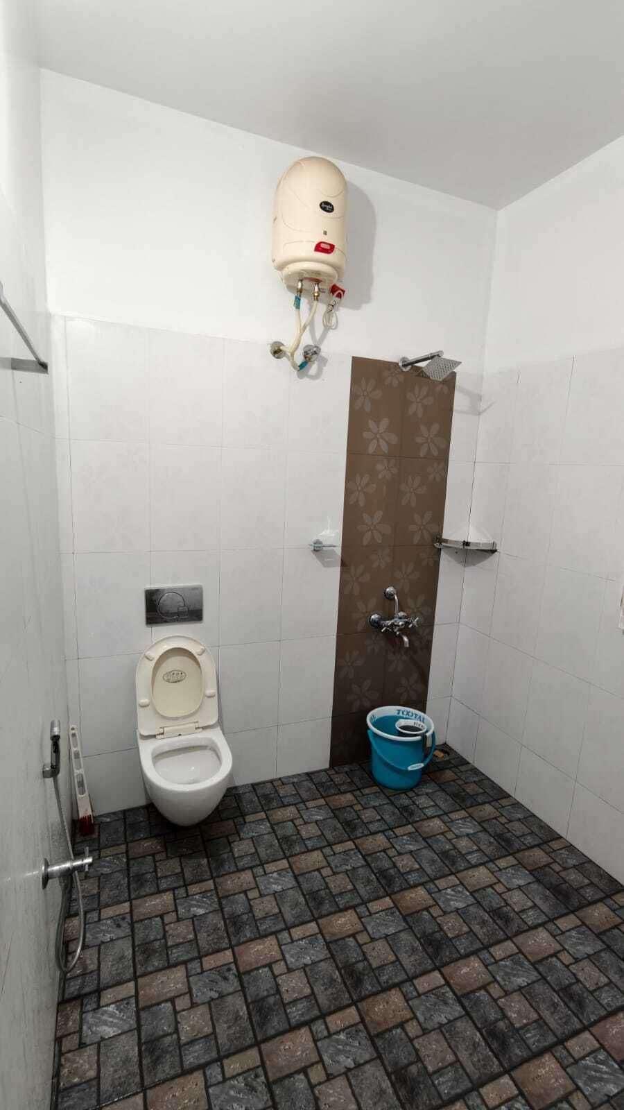 A small bathroom with a toilet, a shower, and a blue bucket.