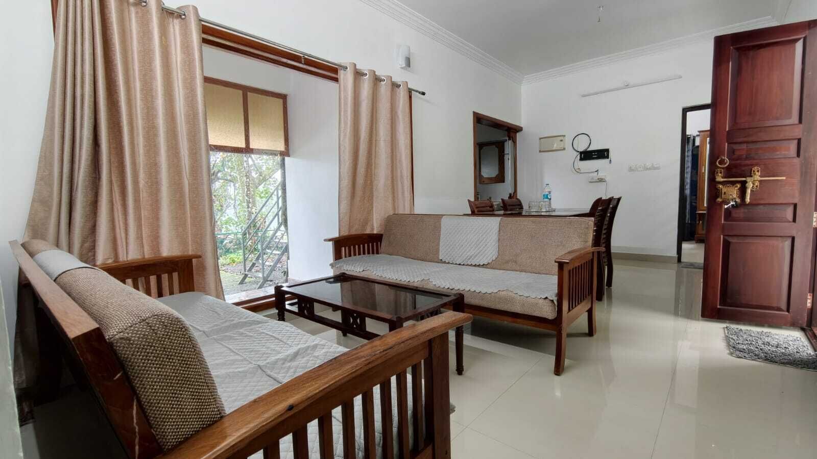 A room with a sofa set, a coffee table, a dining table with chairs, a mirror, and a wooden door.