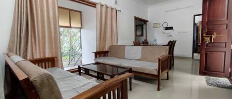 A room with a sofa set, a coffee table, a dining table with chairs, a mirror, and a wooden door.