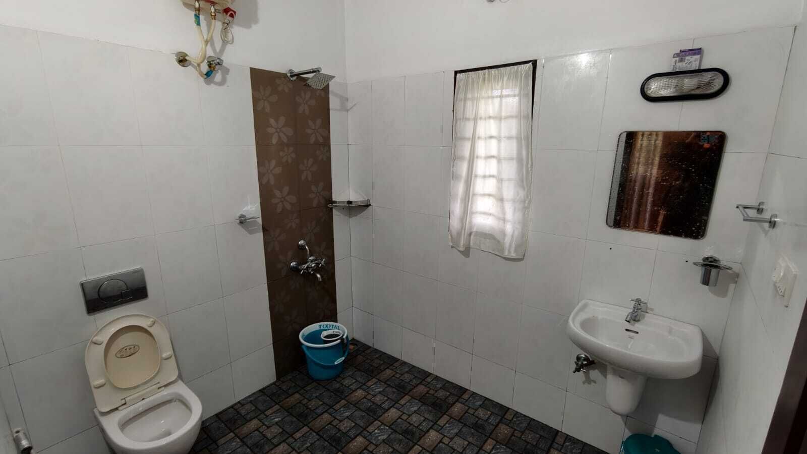 A small bathroom with a toilet, a sink, a shower, and a bucket.