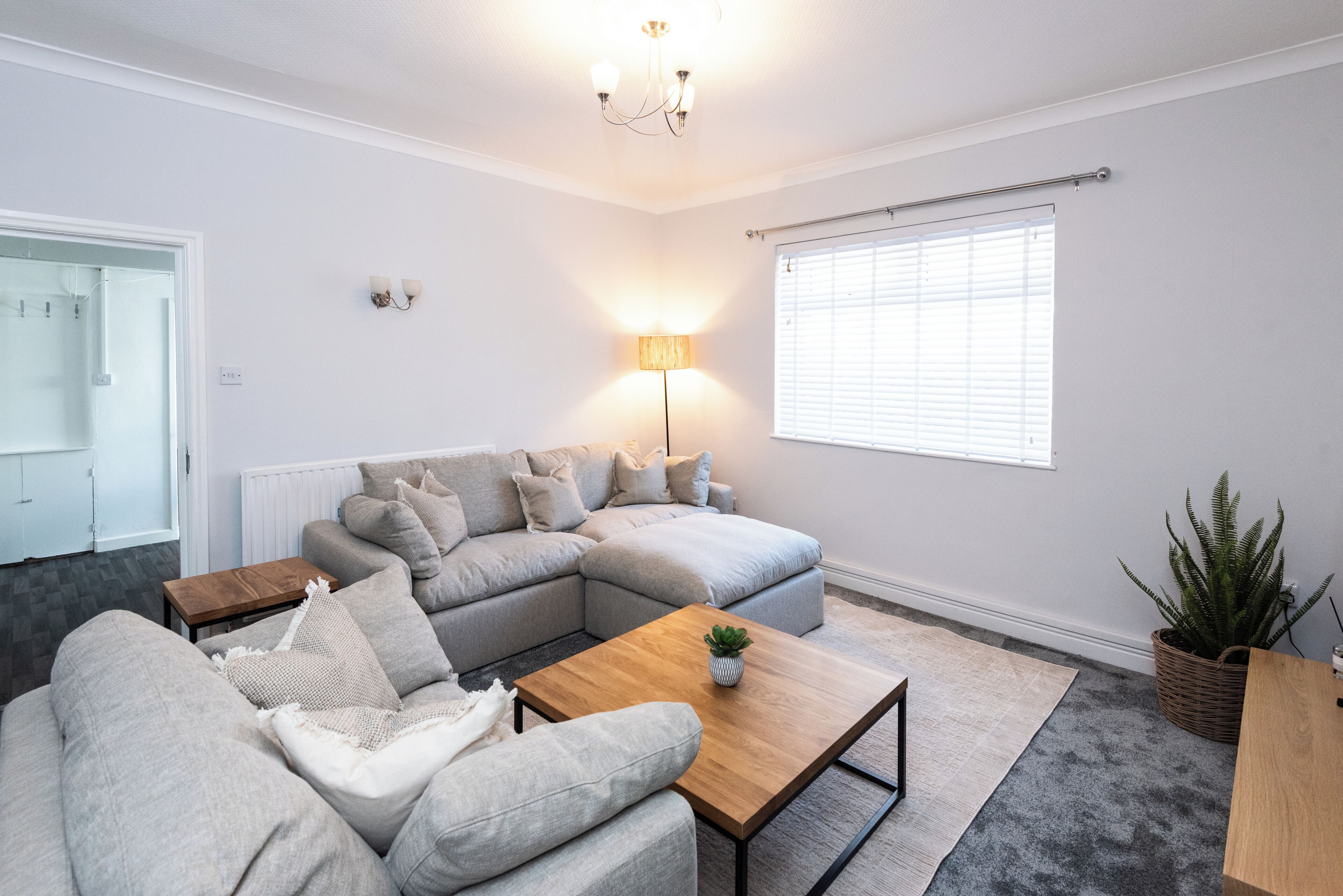 A modern living room with a sectional sofa, a wooden coffee table, a floor lamp, and a large window with blinds.