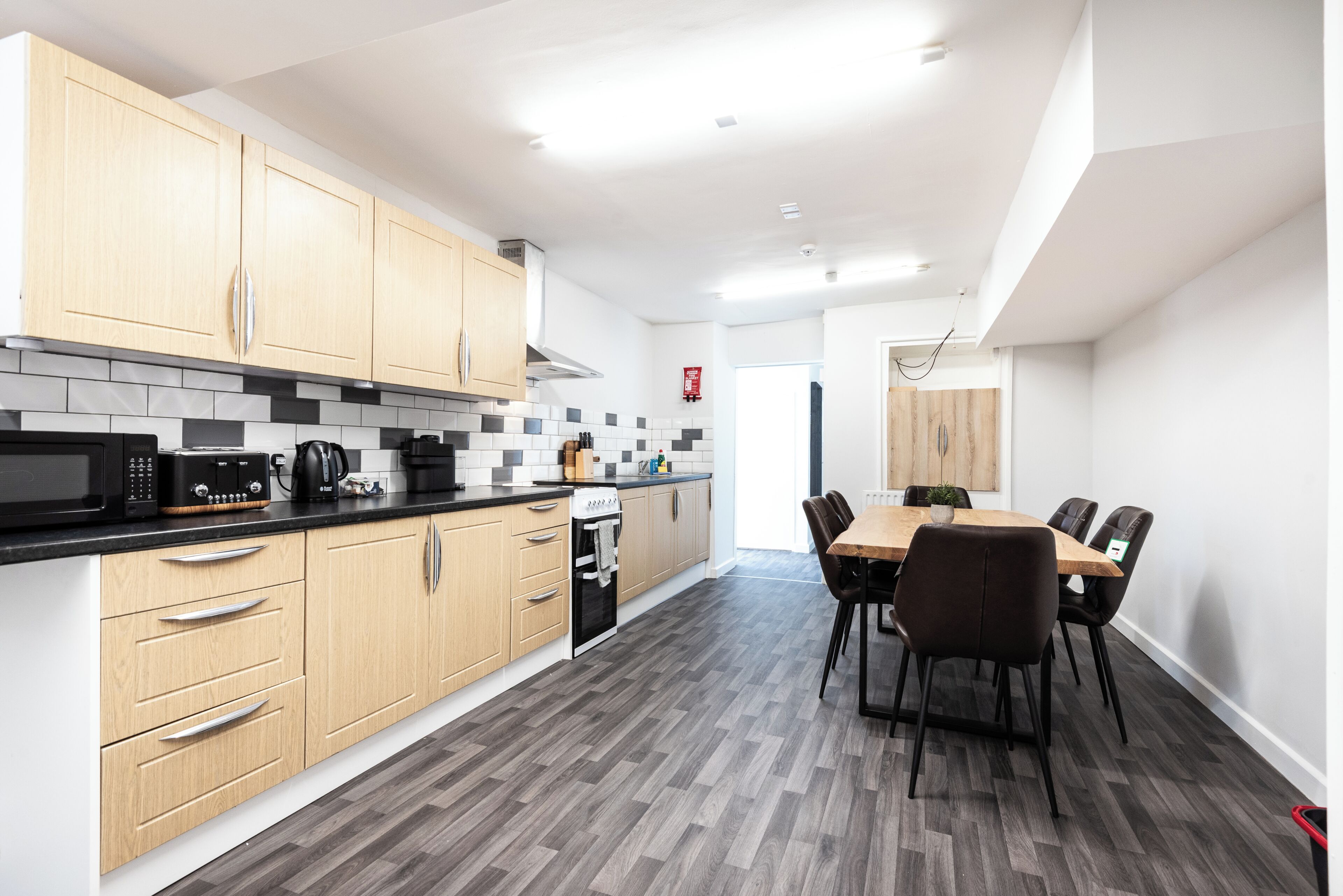 A modern kitchen with wooden cabinets, a black countertop, and a dining area with a table and chairs.