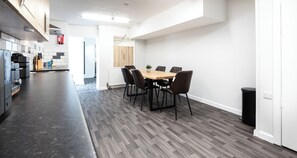 A modern kitchen with a dining area, featuring a herringbone floor pattern, a wooden dining table, and black chairs. - Bayview Apartment by Guestz (Morecambe)