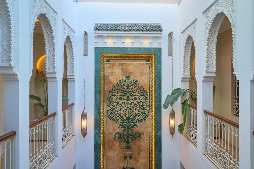 A hallway with ornate white arches and a central door with intricate green patterns.